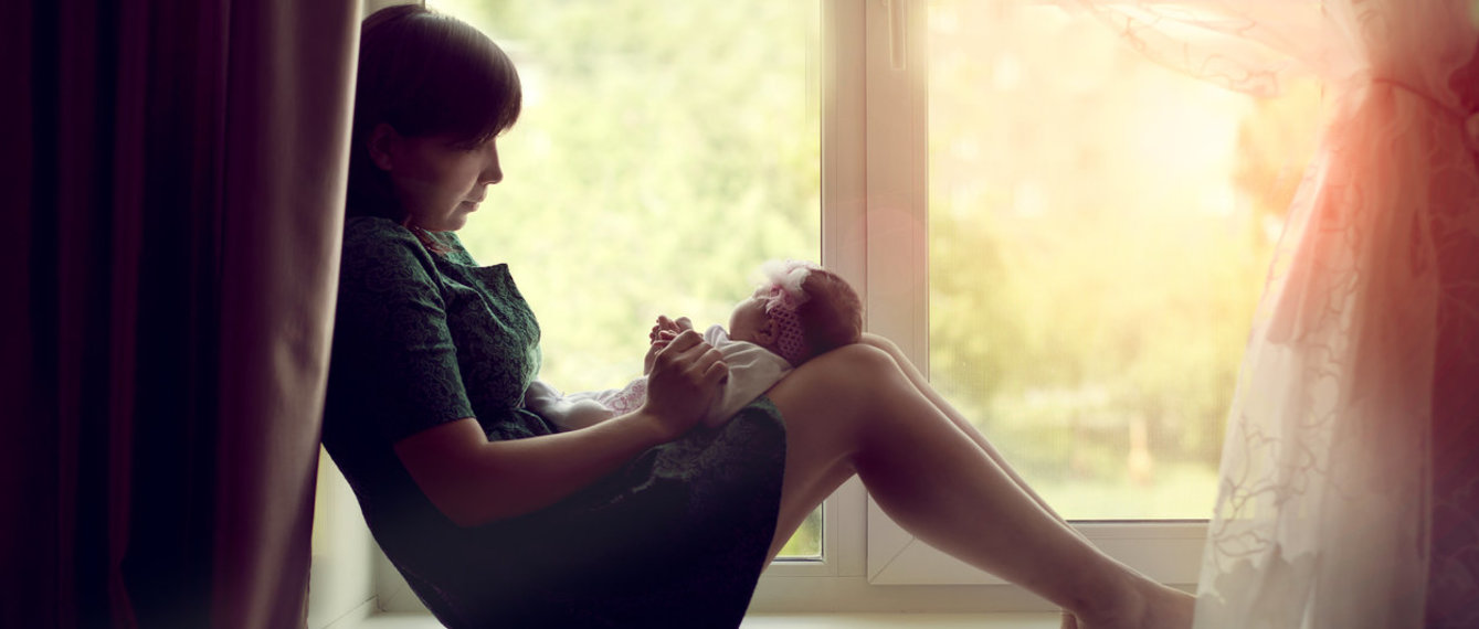 Frau mit Baby alleine am Fenster