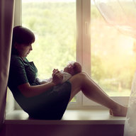 Frau mit Baby alleine am Fenster