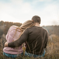 Rückenansicht eines Paares, das in der Wiese sitzt und sich umarmt