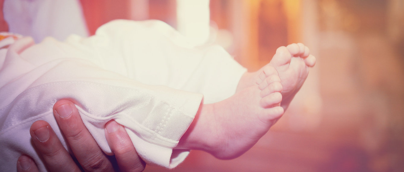 Taufpate hält Baby mit Taufkleid und nackten Füßen
