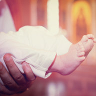 Taufpate hält Baby mit Taufkleid und nackten Füßen