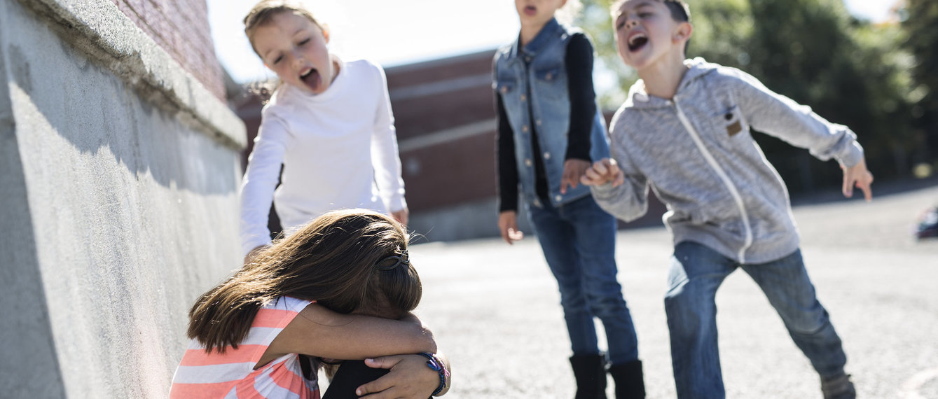 Kinder lachen am bodensitzendes Kind aus