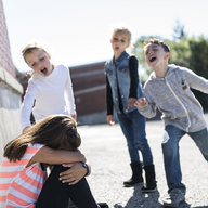 Kinder lachen am bodensitzendes Kind aus
