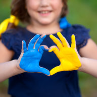 Kind formt mit Farben der Ukraine bemalten Händen ein Herz 