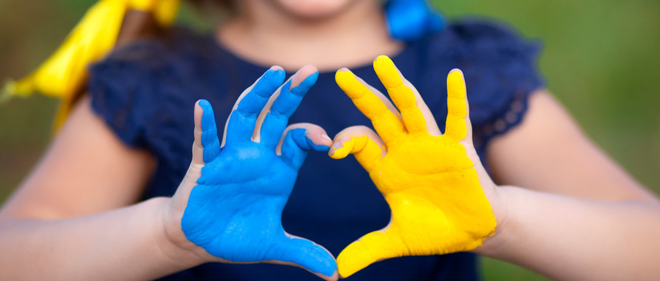 Kind formt mit Farben der Ukraine bemalten Händen ein Herz 