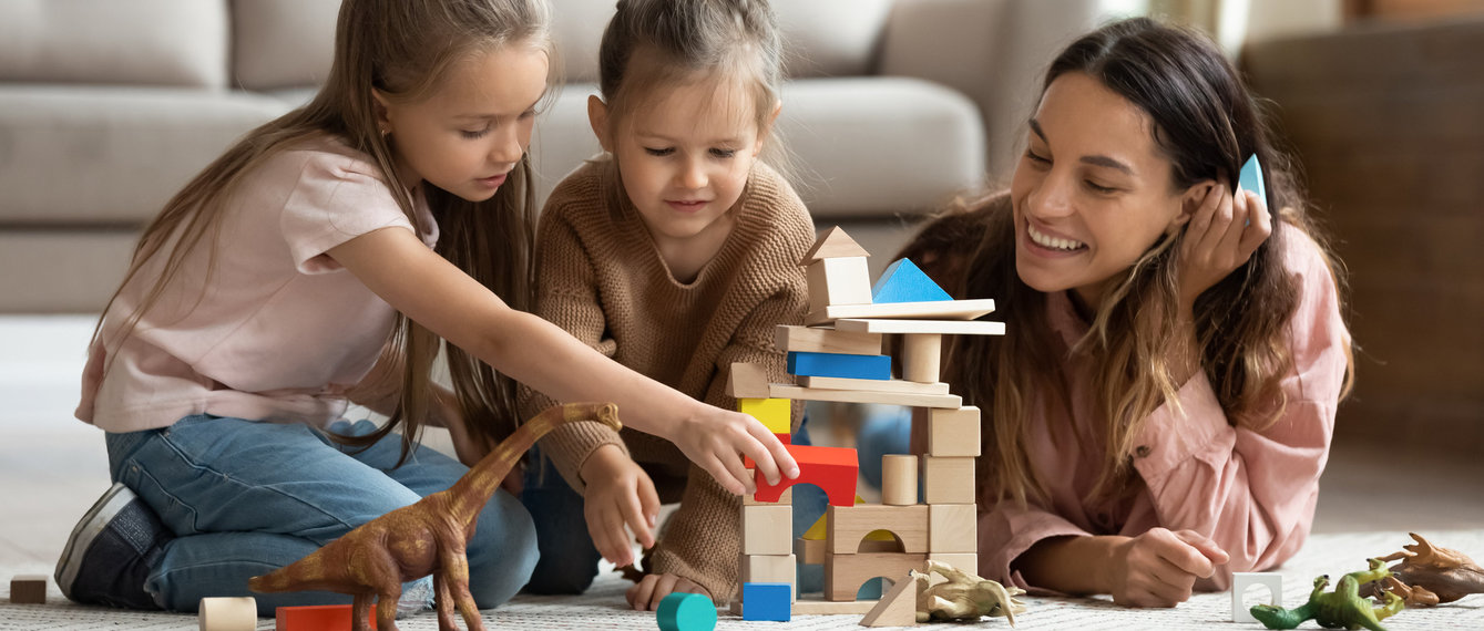 Mutter liegt mit Kindern am Teppich spielt mit Bausteinen