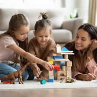 Mutter liegt mit Kindern am Teppich spielt mit Bausteinen
