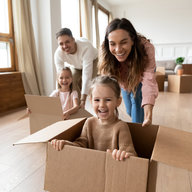Eltern schieben Kinder im Umzugskarton herum