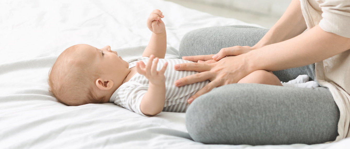 Baby liegt auf Bett, Mutter massiert den Bauch