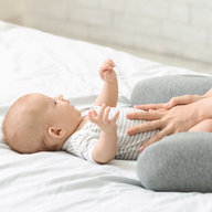 Baby liegt auf Bett, Mutter massiert den Bauch