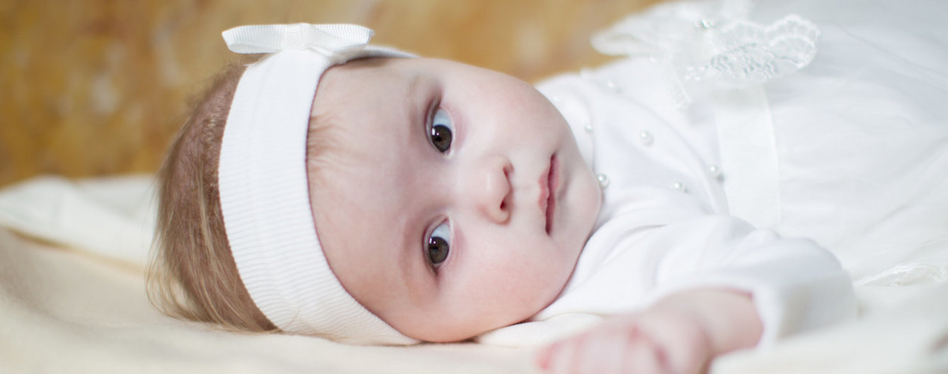 Taufe - Mädchen mit Taufkleid - meinefamilie.at Baby liegt im Taufkleid und mit weißem Stirnband
