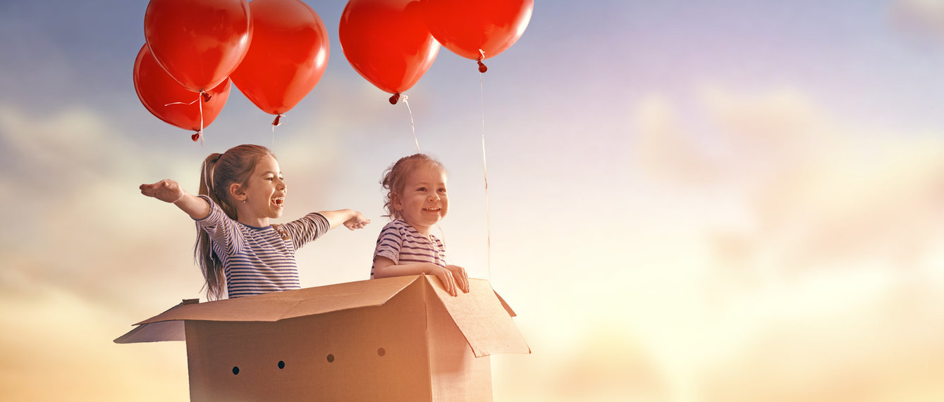 zwei Kinder sitzen in einem Karton mit Lufballons