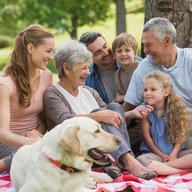 Oma, Opa, Eltern, Kinder und Hund sitzen glücklich auf Picknickdecke
