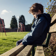 Kleiner Bub sitzt alleine auf Bank am Spielplatz