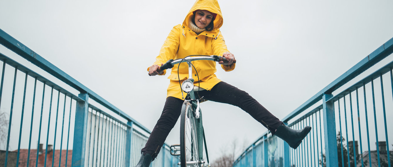 Frau fährt mit Rad im Regen mit gelben Regenmantel