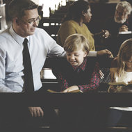Familie mit zwei Kindern sitzt in der Kirchenbank mit Liederbüchern