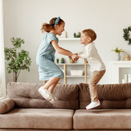 Geschwister hüpfen fröhlich auf einer Couch