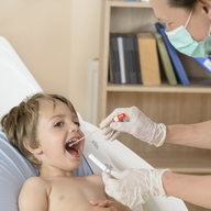 Ärztin macht einen Rachenabstrich bei einem kleinem Buben