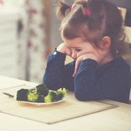 Unglückliches Mädchen vor einem Teller Brokkoli
