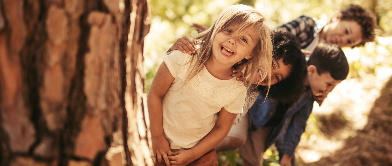 Kinder spielen Verstecken hinter dem Baumstamm