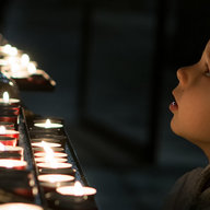 Kleiner Bub in dunkler Kirche vor Teelichtern, die angezündet sind, von Seite zu sehen