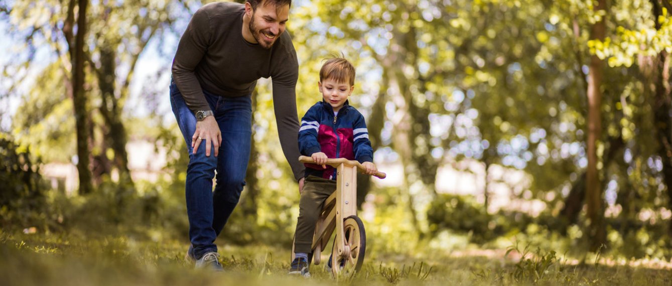 Vater hilft kleinem Sohn beim Radfahren im Wald