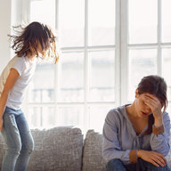 Genervte Mutter mit Tochter die am Sofa hüpft