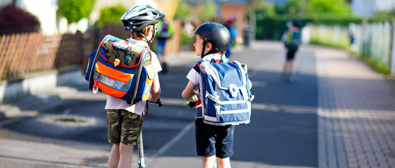 Schulkinder mit Scootern und Schultaschen am Schulweg