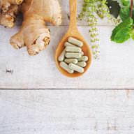 Kräuterpillen auf Holzlöffel und grünes Kraut