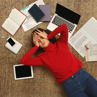 Mädchen liegt mit Schulunterlagen überfordert am Boden