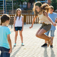 Glückliche Kinder springen im Schulhof über ein Springseil.