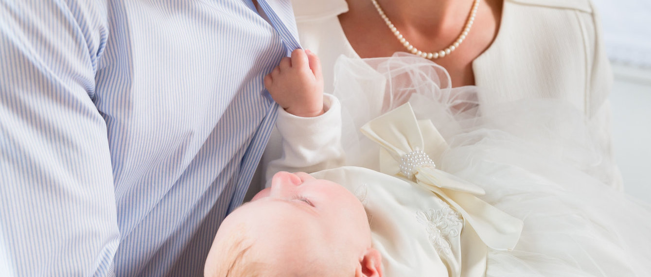 Vater und Mutter halten das Taufkind im weißen Taufkleid bei der Tauffeier