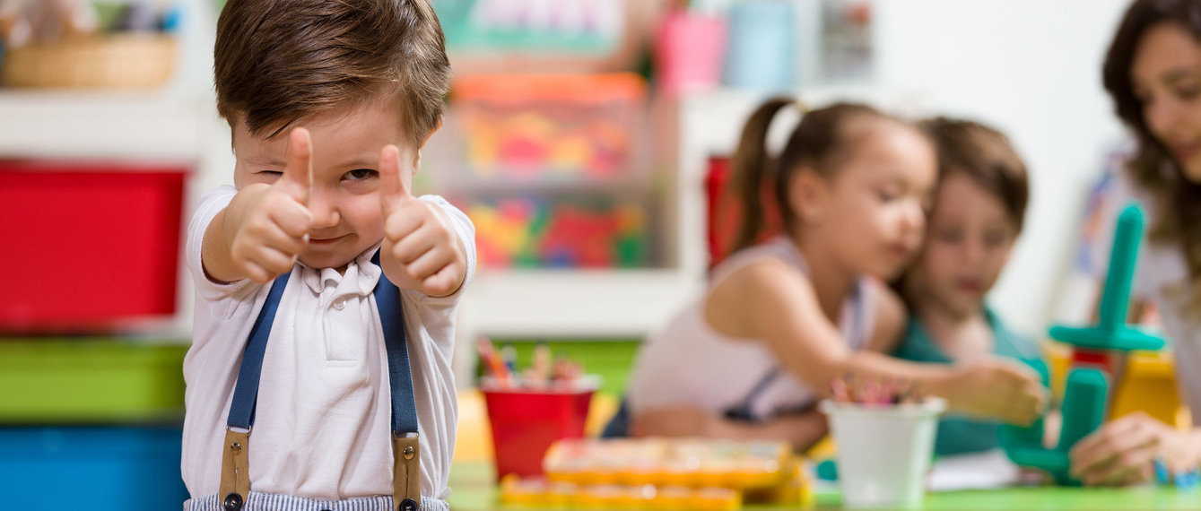 Bub im Kindergarten zeigt erhobenen Daumen