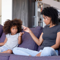 Mutter sitzt mit Tochter auf der Couch, beide schimpfen