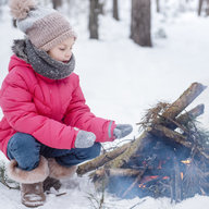 Kind sitzt im Schnee neben Lagerfeuer