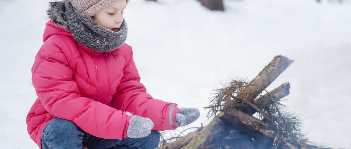 Kind sitzt im Schnee neben Lagerfeuer