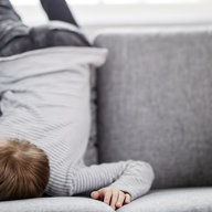 Kind liegt demotiviert auf Couch