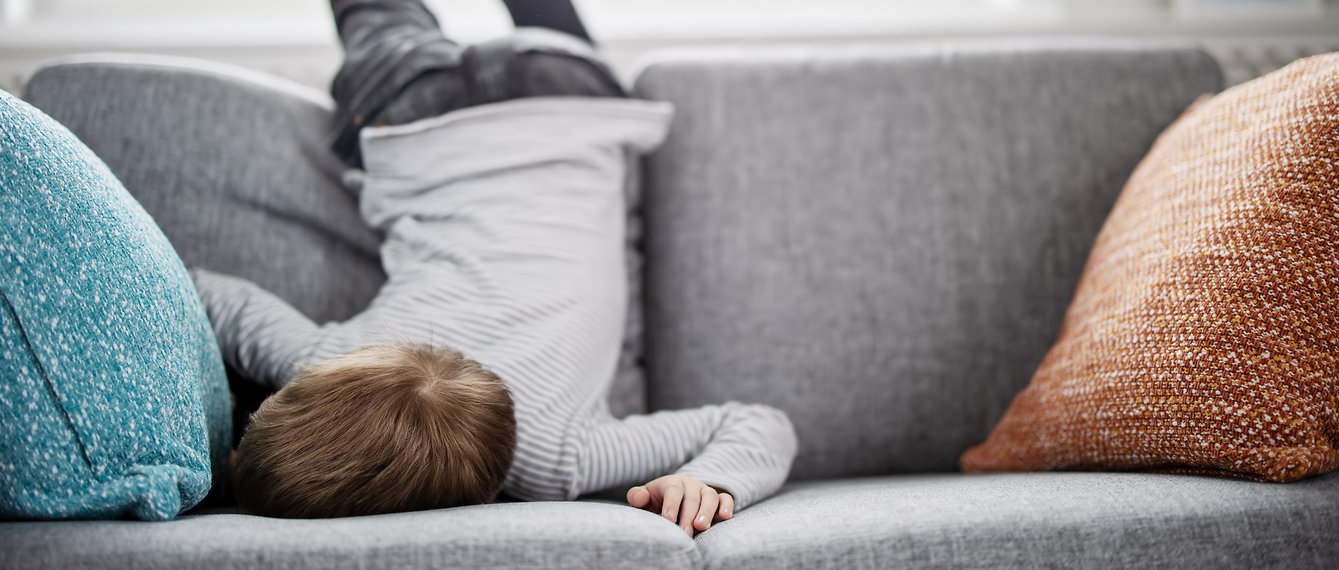 Kind liegt demotiviert auf Couch