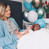 Mutter liegt mit Baby im Bett, im Hintergrund Geschenke