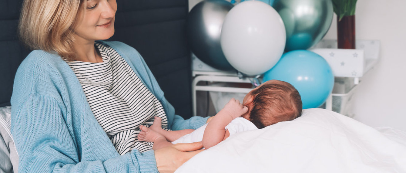 Mutter liegt mit Baby im Bett, im Hintergrund Geschenke