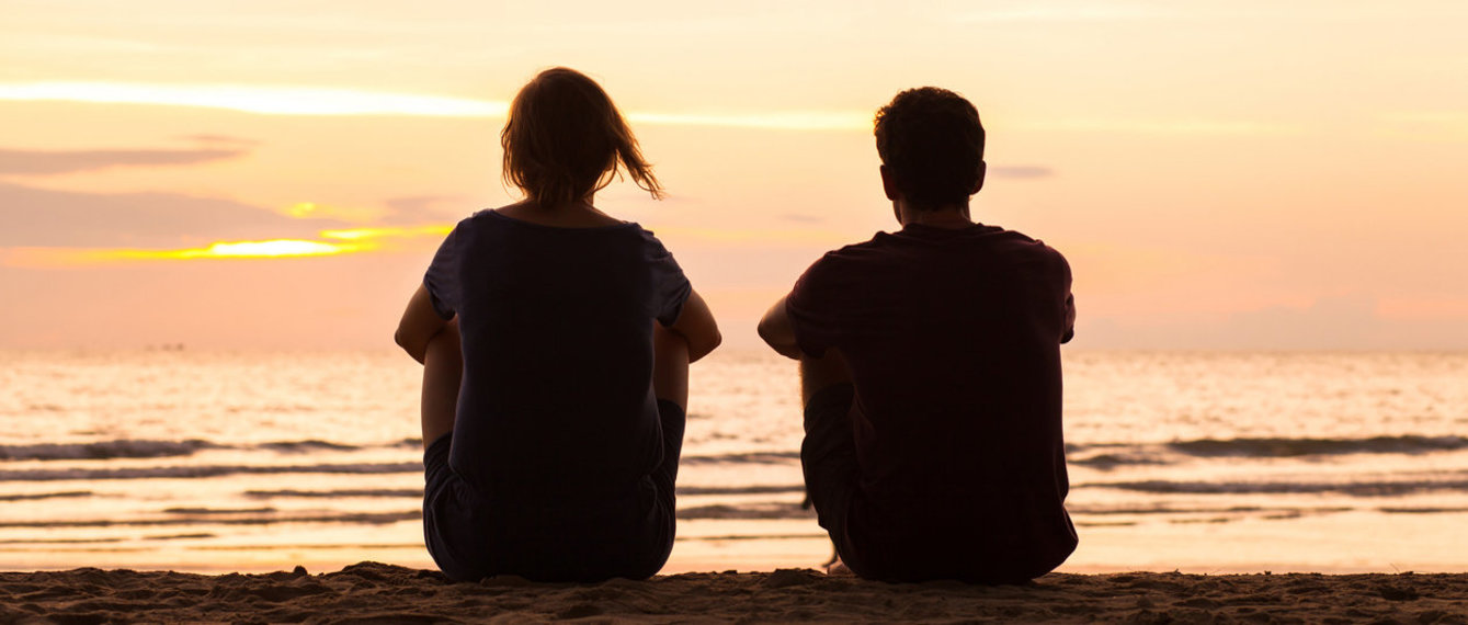 Paar sitzt nebeneinander und schaut aufs Meer