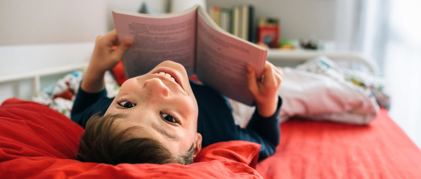 Volksschulkind liegt mit Buch am Bett