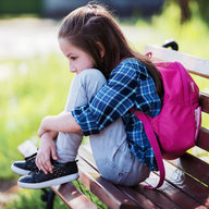 Schulmädchen sitzt traurig auf Bank