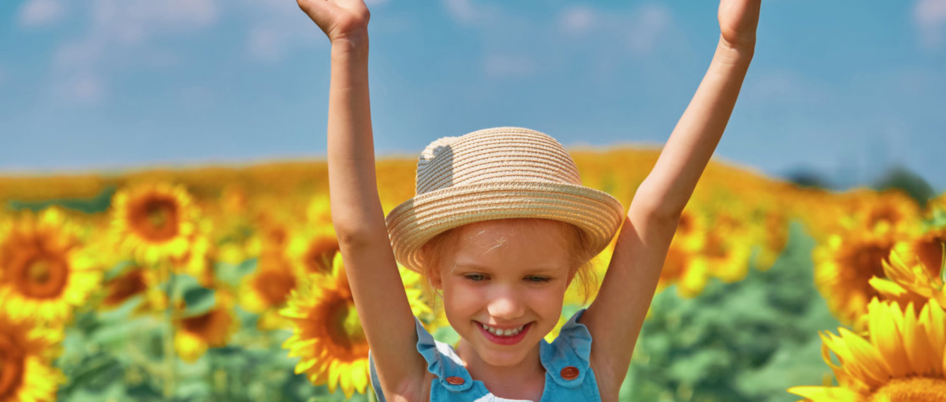 Mädchen mit Hut freut sich in einem Sonnenblumenfeld 