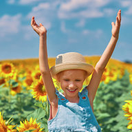 Mädchen mit Hut freut sich in einem Sonnenblumenfeld 