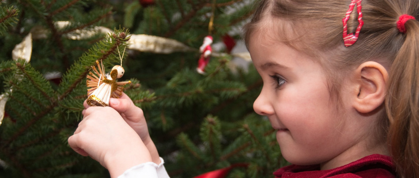 Mädchen betrachtet Engelsfigur am Christbaum