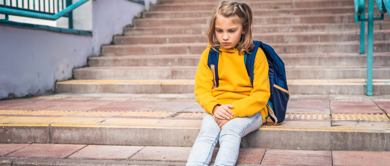 Kind sitzt vor der Schule und wartet abgeholt zu werden