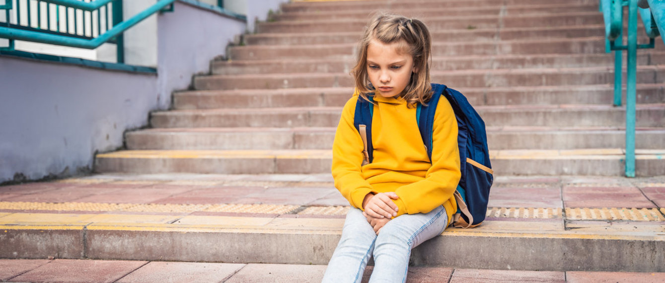 Kind sitzt vor der Schule und wartet abgeholt zu werden