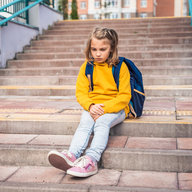 Kind sitzt vor der Schule und wartet abgeholt zu werden