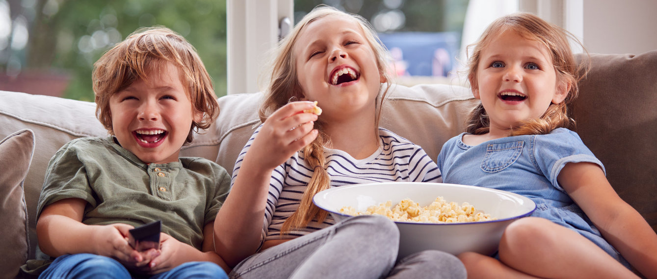 Drei Kinder sitzen vorm Fernseher und essen Popcorn